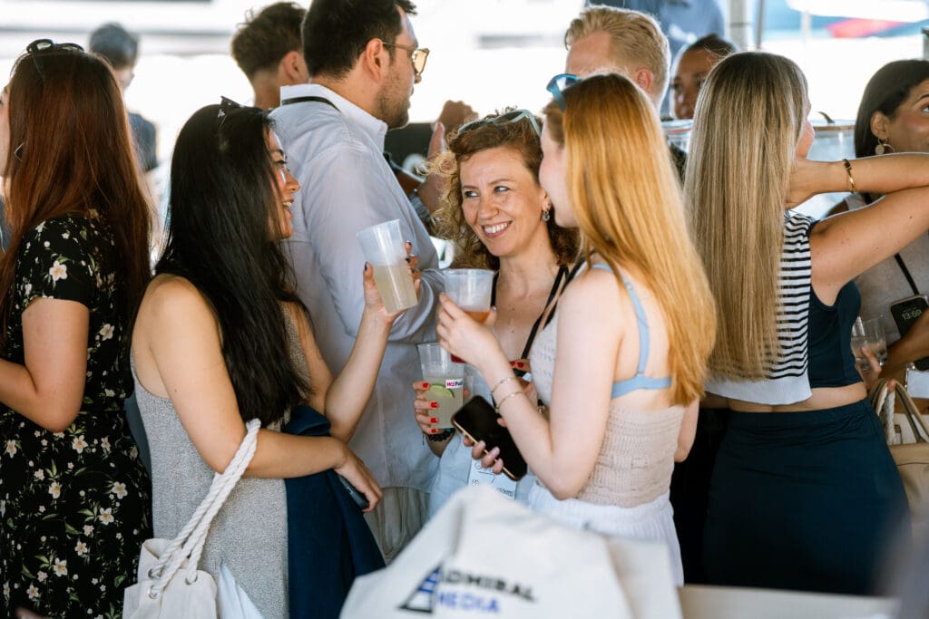 A cluster of guests networking on deck, an Admiral Media tote bag visible.