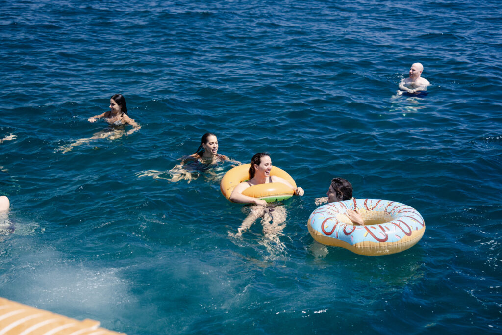 Swimmers floating with rings in deep blue water beside the boat.
