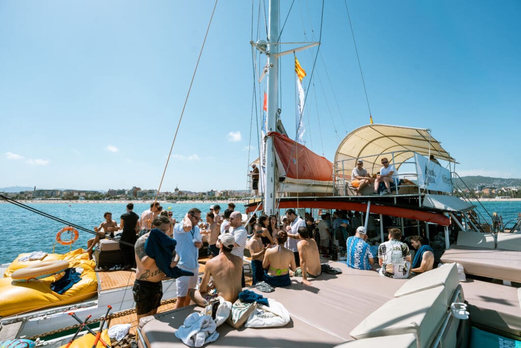 Guests filling the deck of the catamaran with the Barcelona coastline behind.