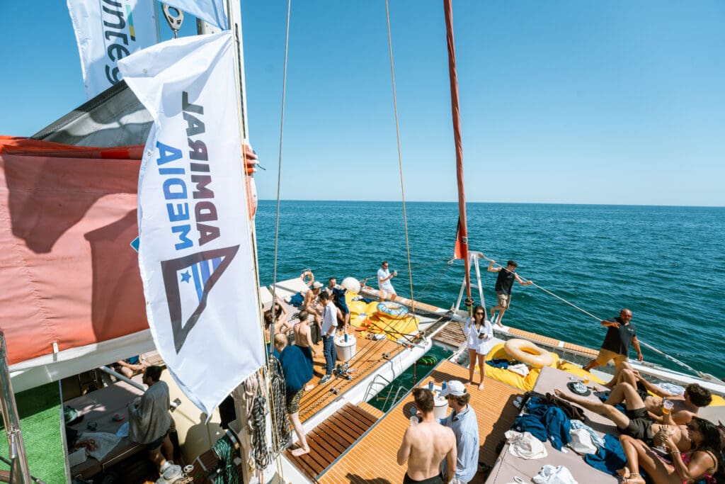 The Admiral Media flag flying over a packed deck above turquoise water.